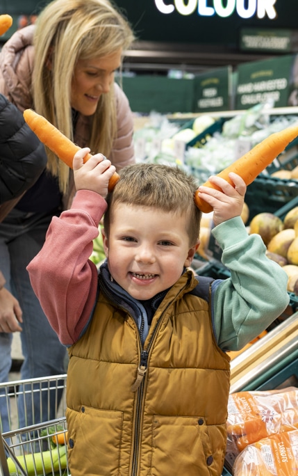 Young boy holding up carrots like ears in a supermarket looking cheeky