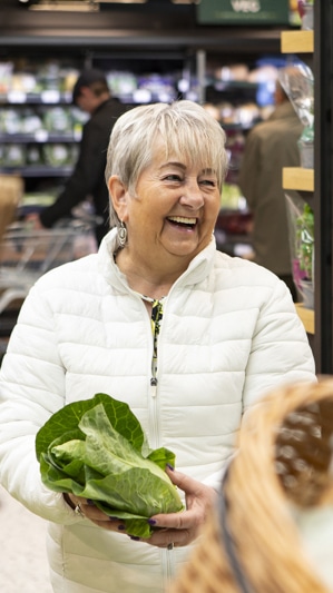 Woman in her senior years widely smiling in a supermarket holding a sweetheart cabbage